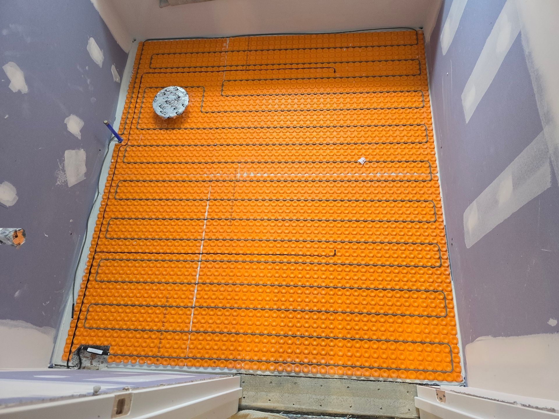 Orange heated floor mat installed in a bathroom, wires connected to a control.