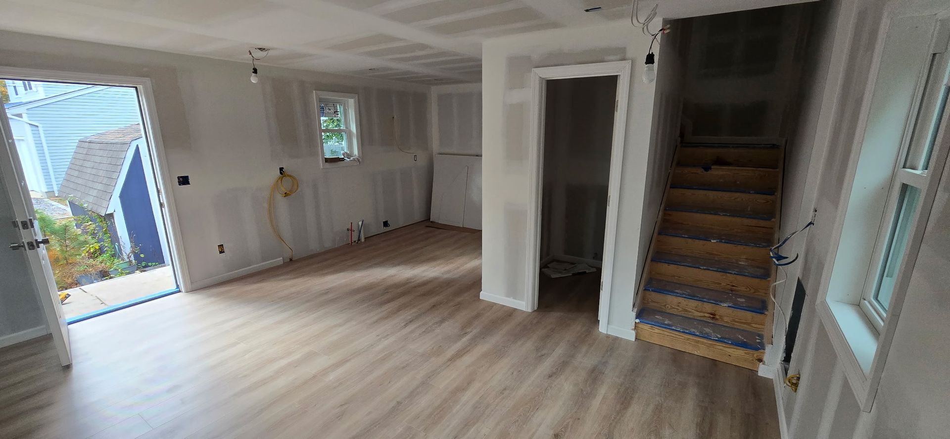 Interior view of a room under construction with wood flooring, unfinished walls, and a staircase.