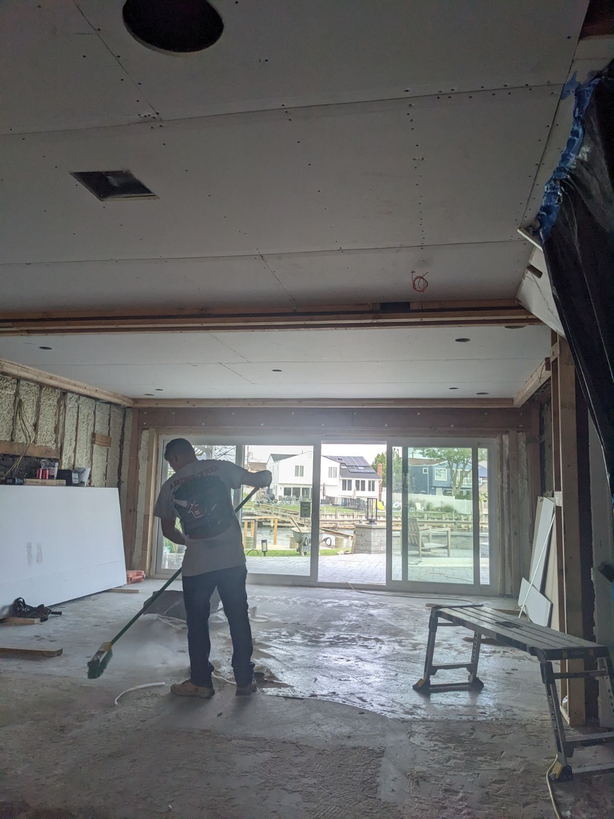 Person cleaning a concrete floor in a room under construction with sliding glass doors.