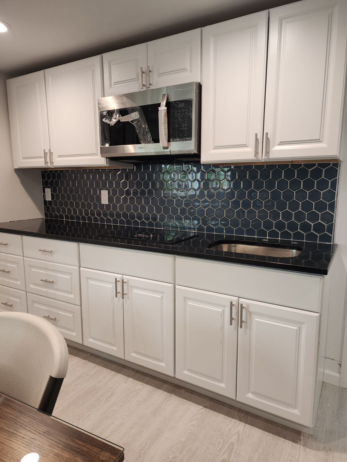 White kitchen cabinets, black countertop, hexagon tile backsplash, stainless steel microwave, and sink.