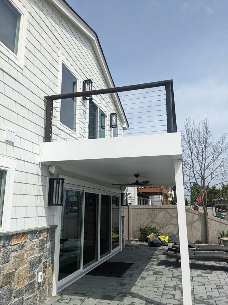Exterior of a house with a second-story balcony and lower-level patio. White siding and a cable railing are visible.