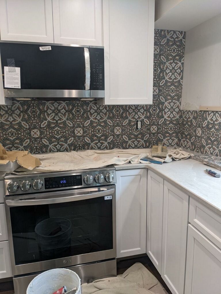 Kitchen with white cabinets, patterned backsplash, stainless steel appliances, and a countertop.