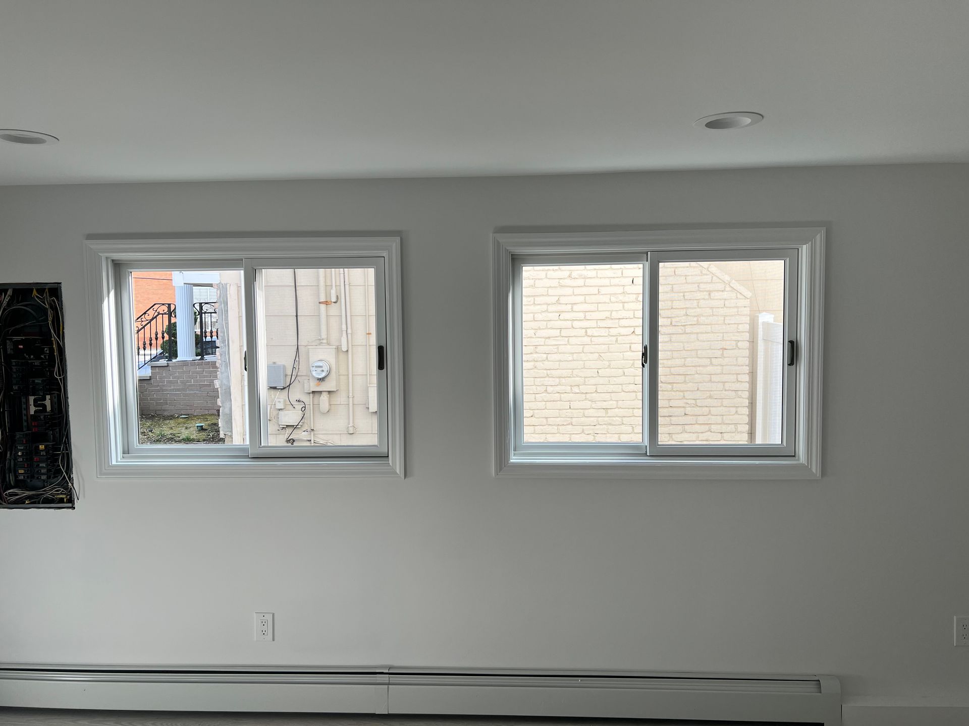 Two white-framed sliding windows on a gray wall. One reveals a street, the other a brick wall.