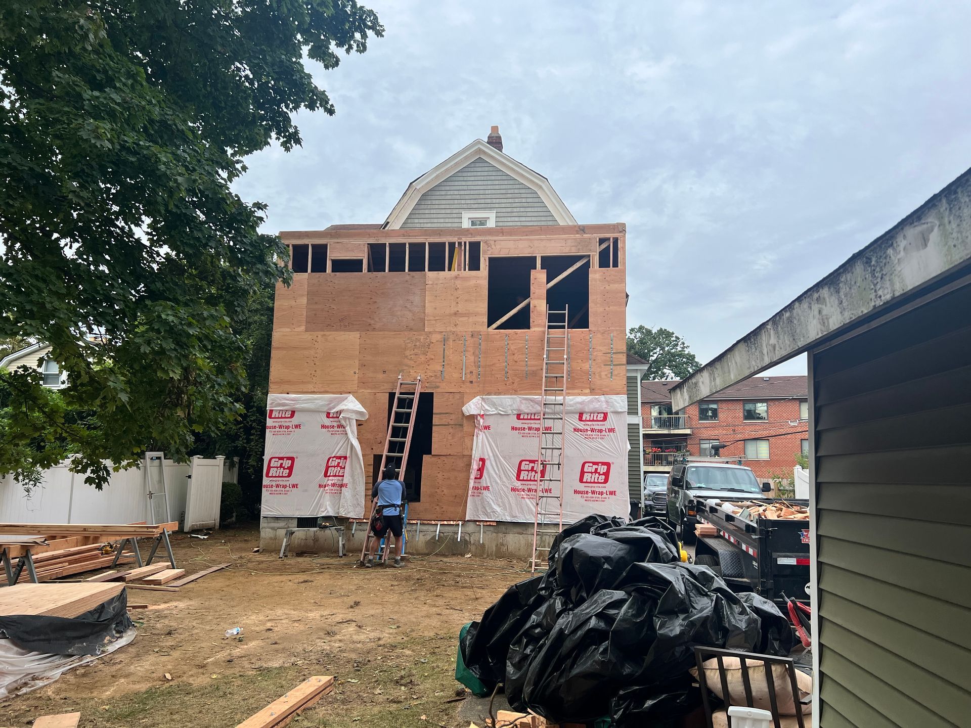Building under construction; wood framing and sheathing visible. Person on ladder. Cloudy sky.