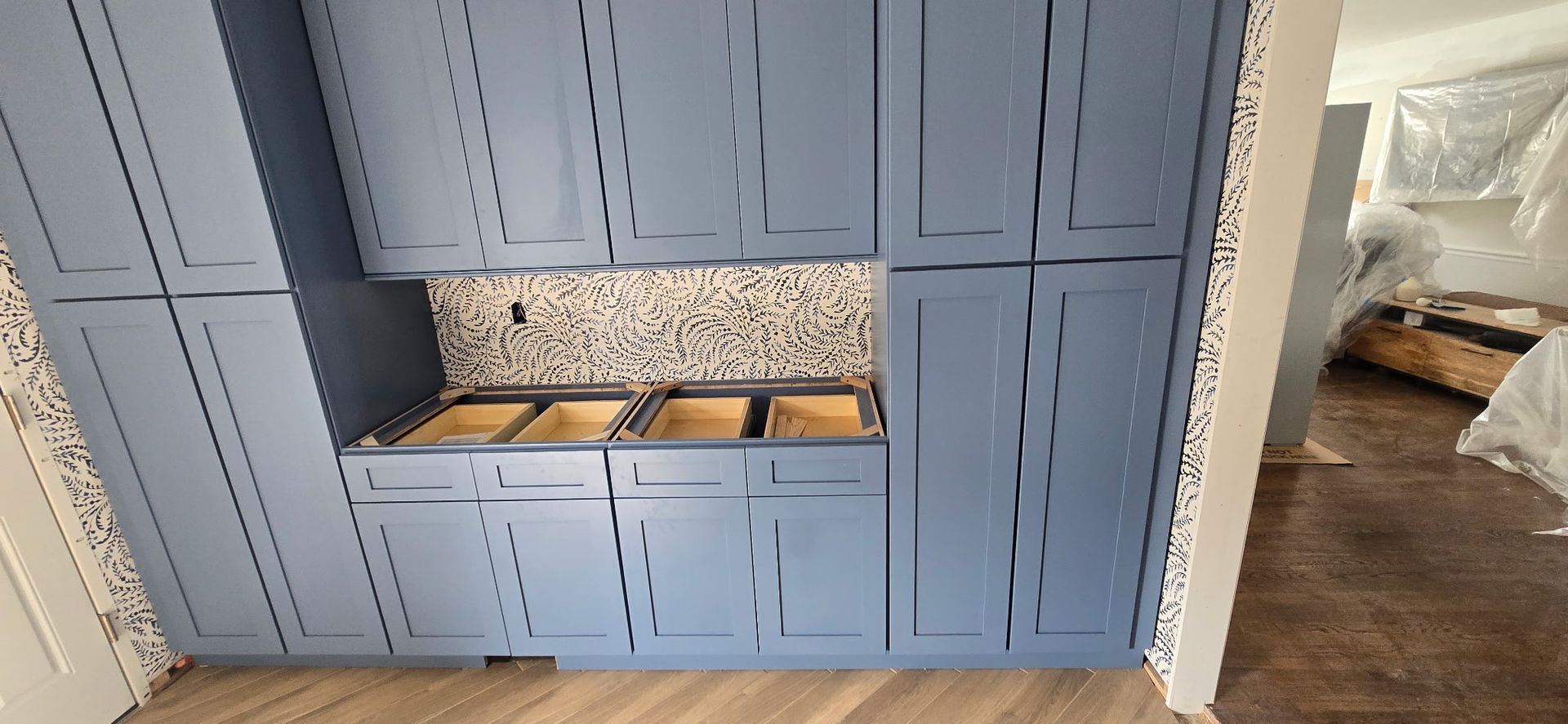 Blue kitchen cabinets with unfinished countertops, and a tiled backsplash, in a room under construction.