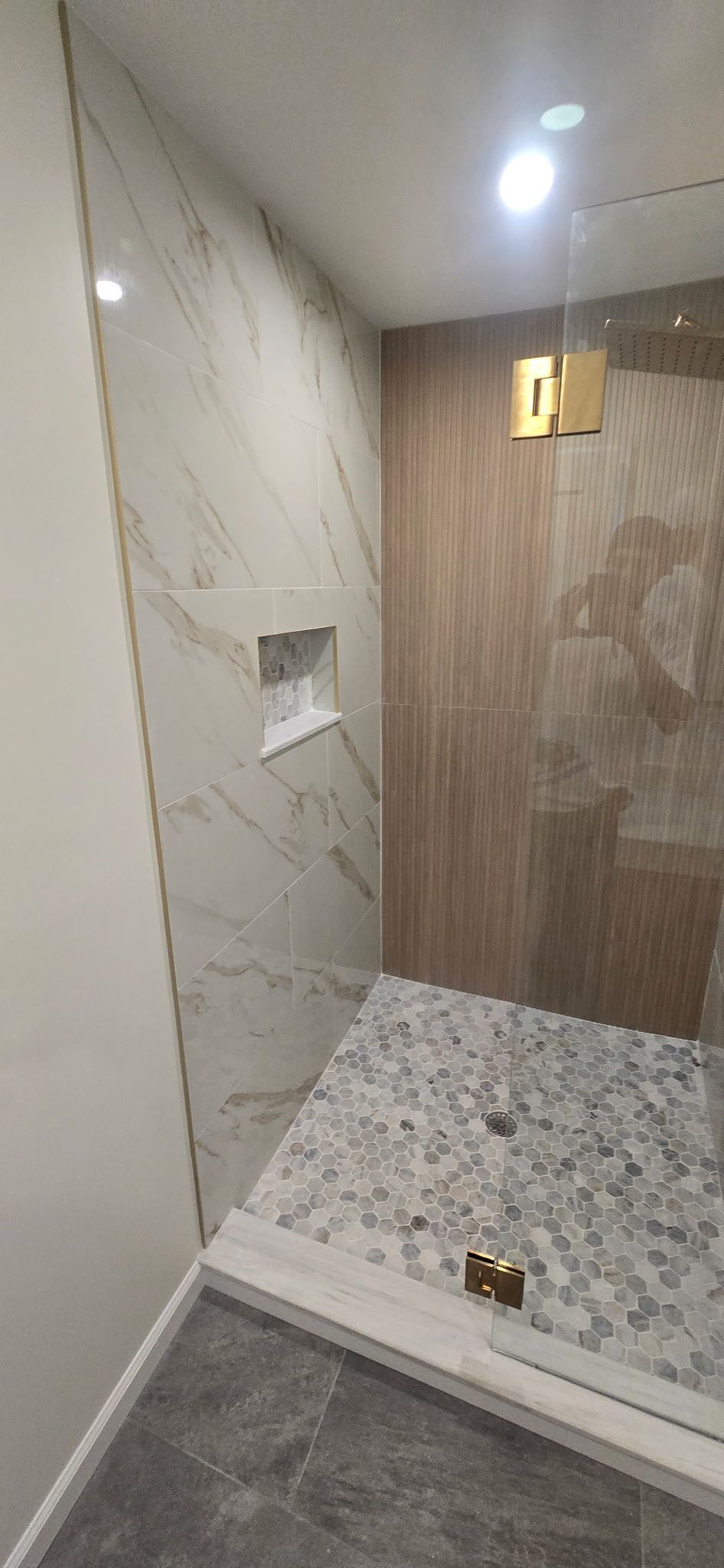 A modern bathroom shower with patterned tile walls and pebble floor.