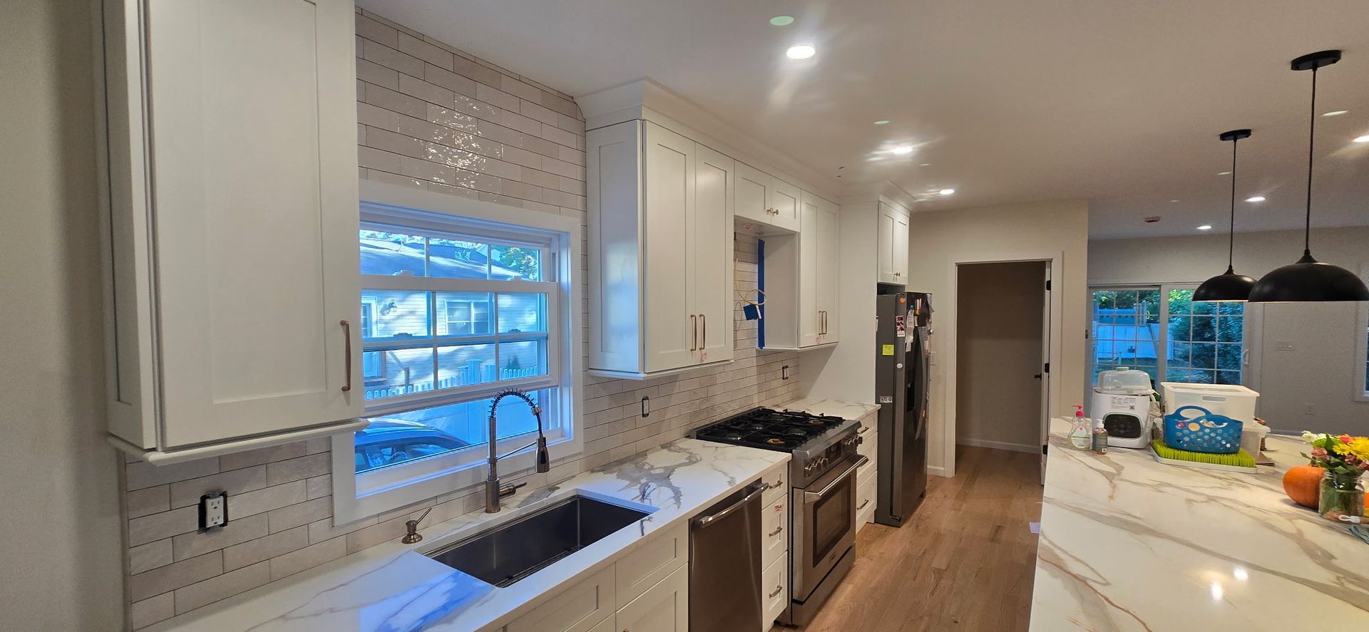 Modern kitchen with white cabinets, marble countertops, stainless steel appliances, and a window.