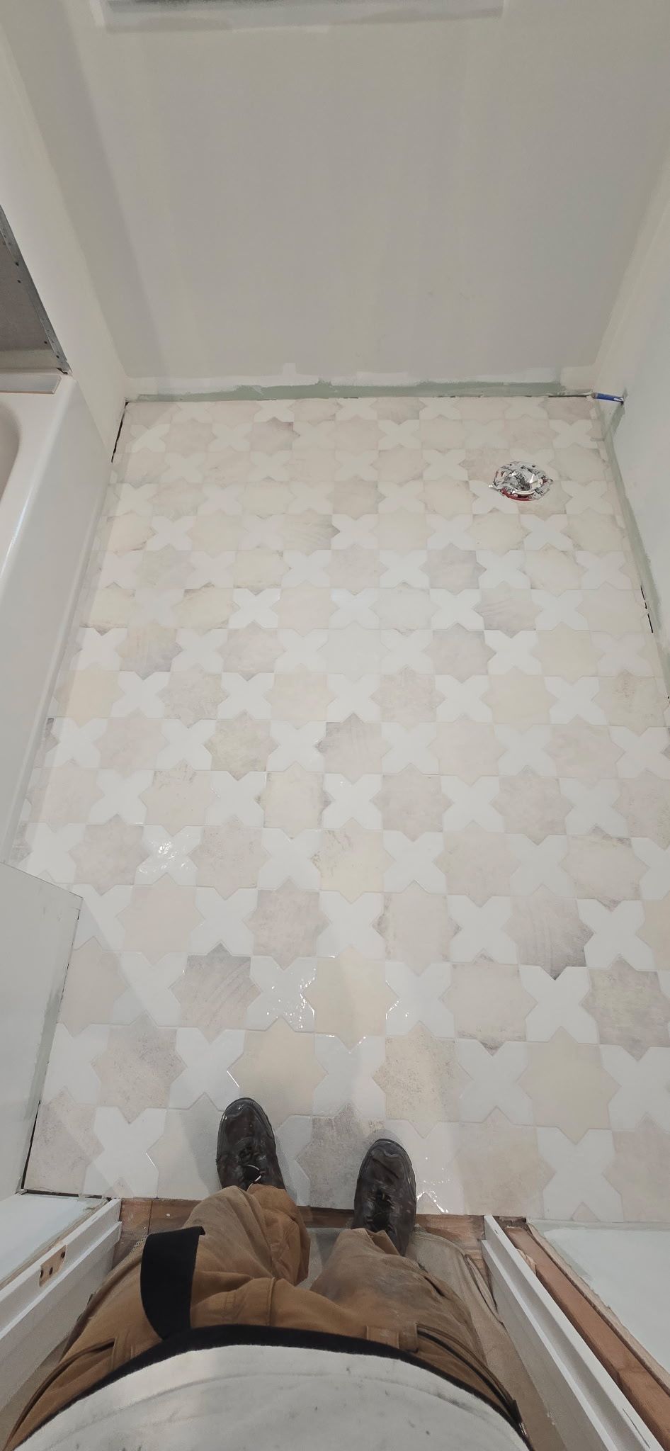 Bathroom floor with patterned tiles being installed. Person standing near entrance.