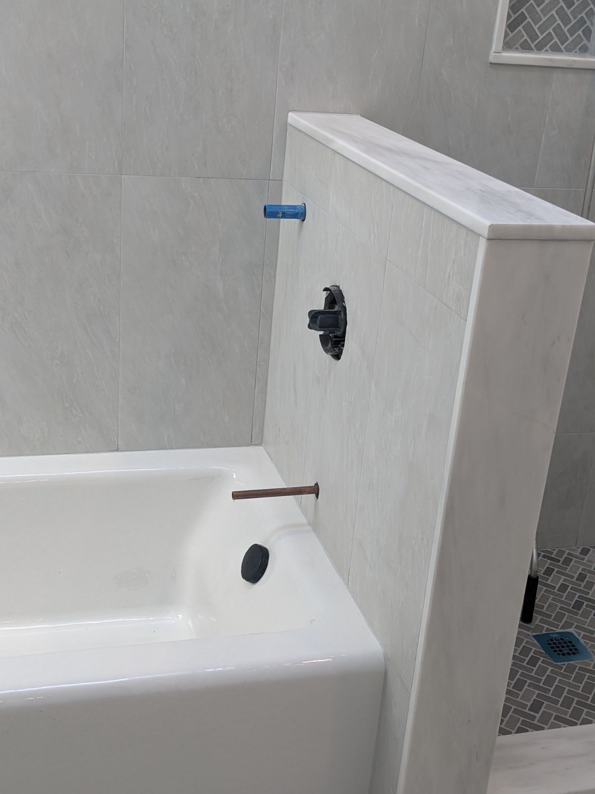 Bathtub with plumbing fixtures installed in a tiled wall; a partially finished bathroom.