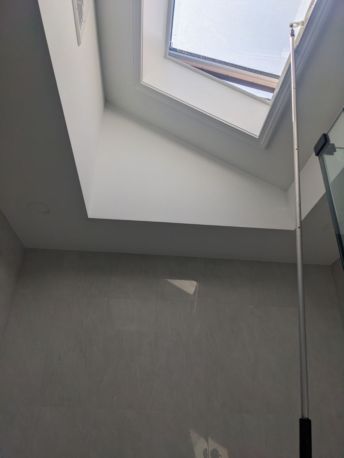 Skylight in a white-walled room; a long pole extends toward the opening, possibly for adjustment.