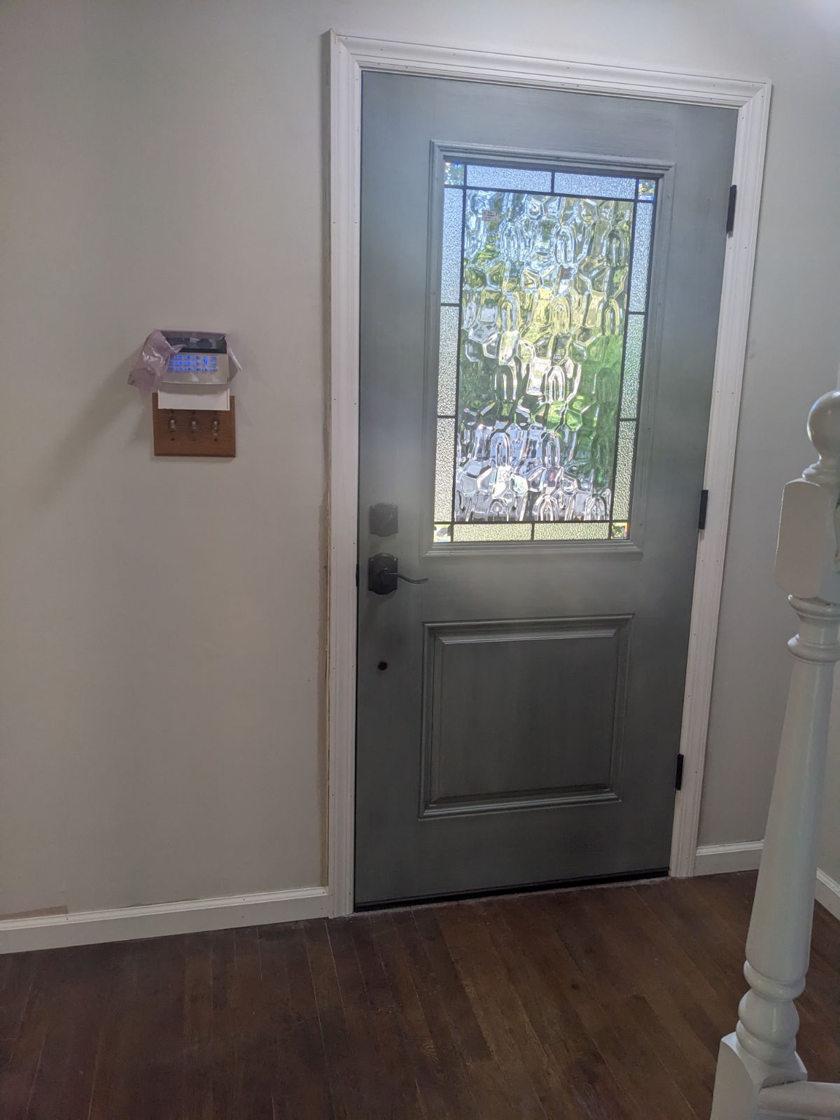 A gray front door with stained glass, white trim, and a small wooden wall organizer.