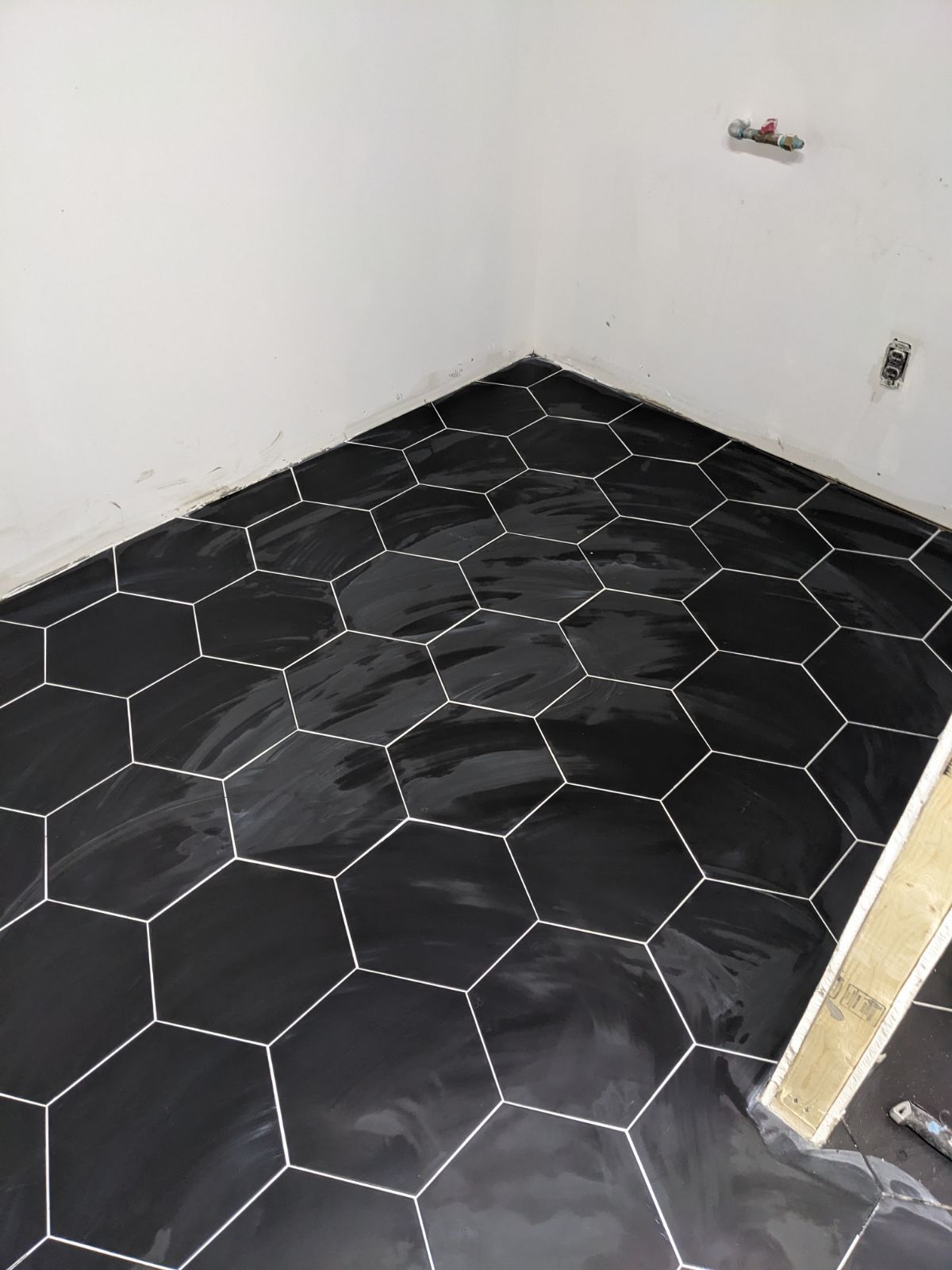 Black hexagonal tiles with white grout on a bathroom floor, against white walls.
