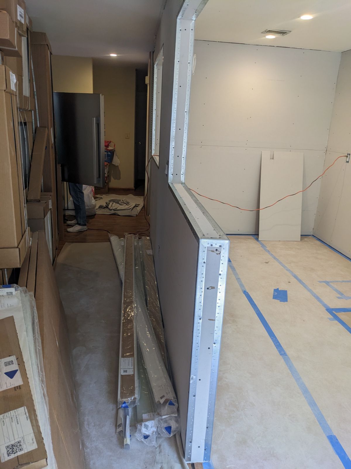 Construction site: partially built room with drywall and framing, supplies on floor, blue tape, and a refrigerator.