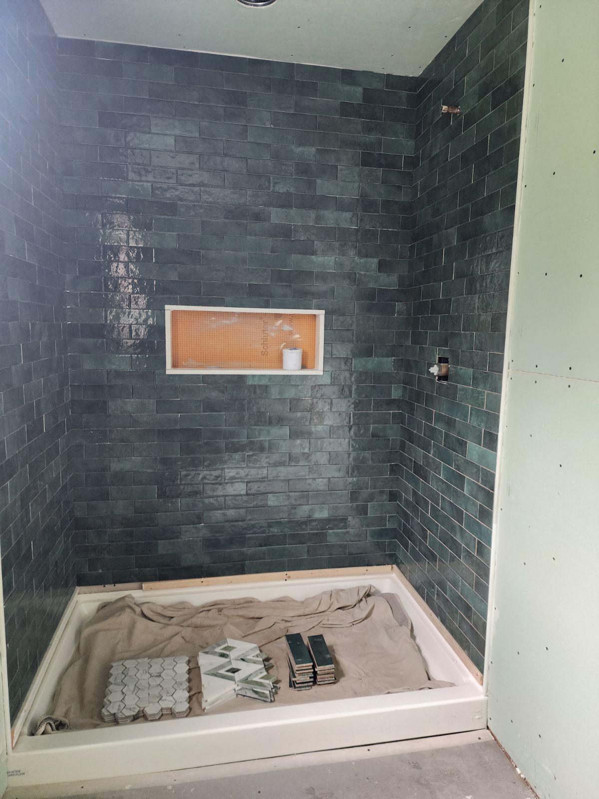 Shower with dark teal brick tiles, a recessed shelf, and a white shower pan.