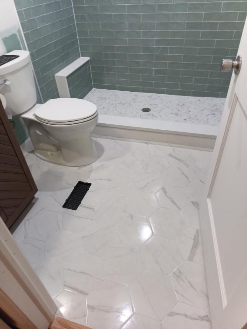 Bathroom with white and gray marble tile floor, green tiled shower, and white toilet.