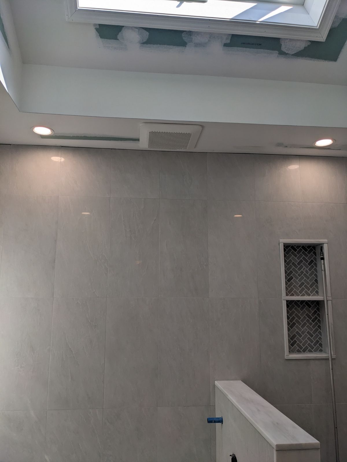 Bathroom wall with tile, lights, a vent, and a small window.