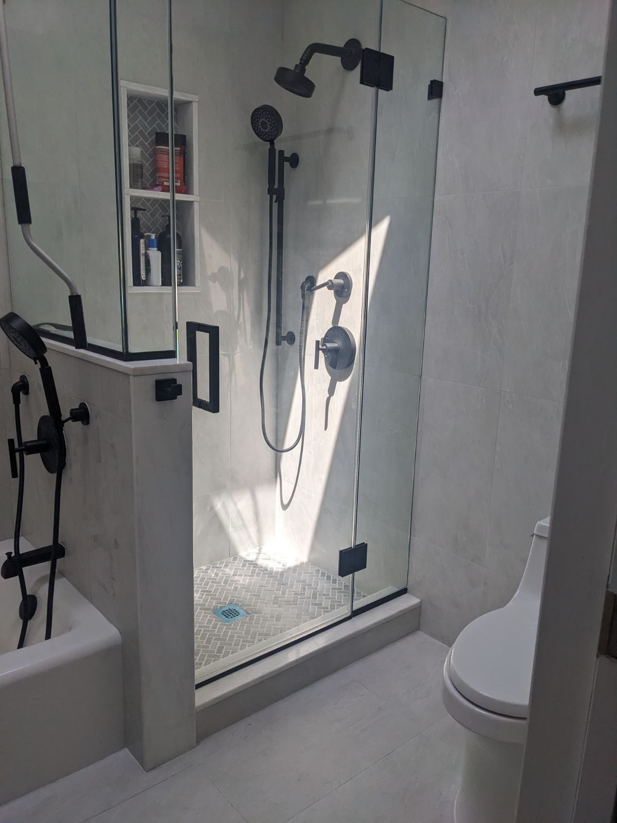 Modern bathroom with walk-in shower. Glass doors, black fixtures, built-in shelving, and a toilet.