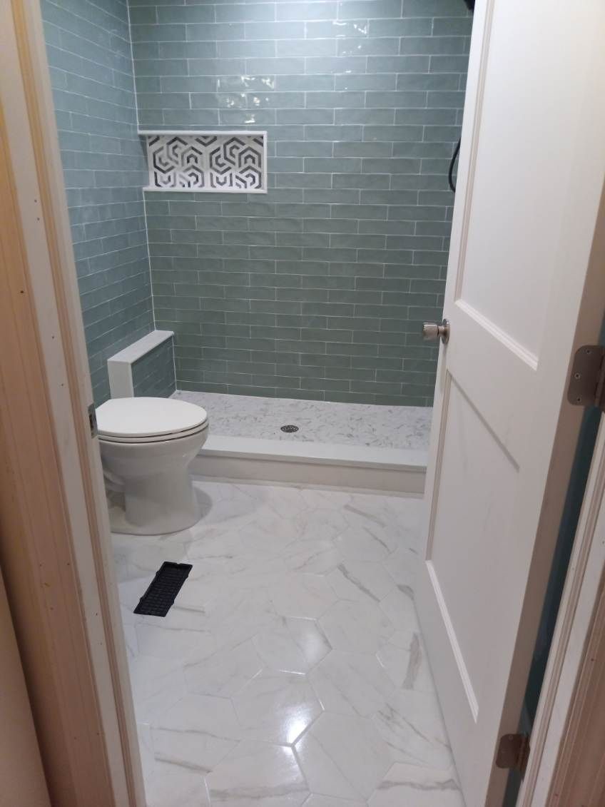 Bathroom with green tiled shower, white toilet and floor, viewed through an open door.