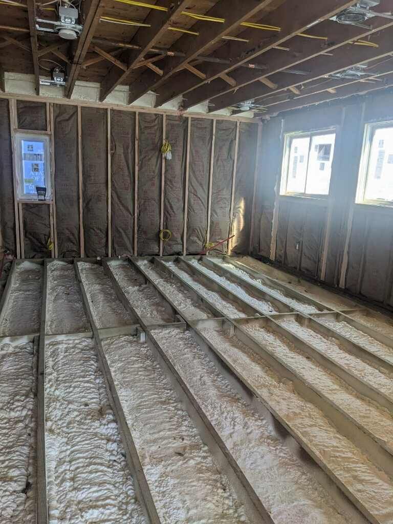 Interior framing of a room under construction with exposed wooden beams, insulation, and partially finished flooring.