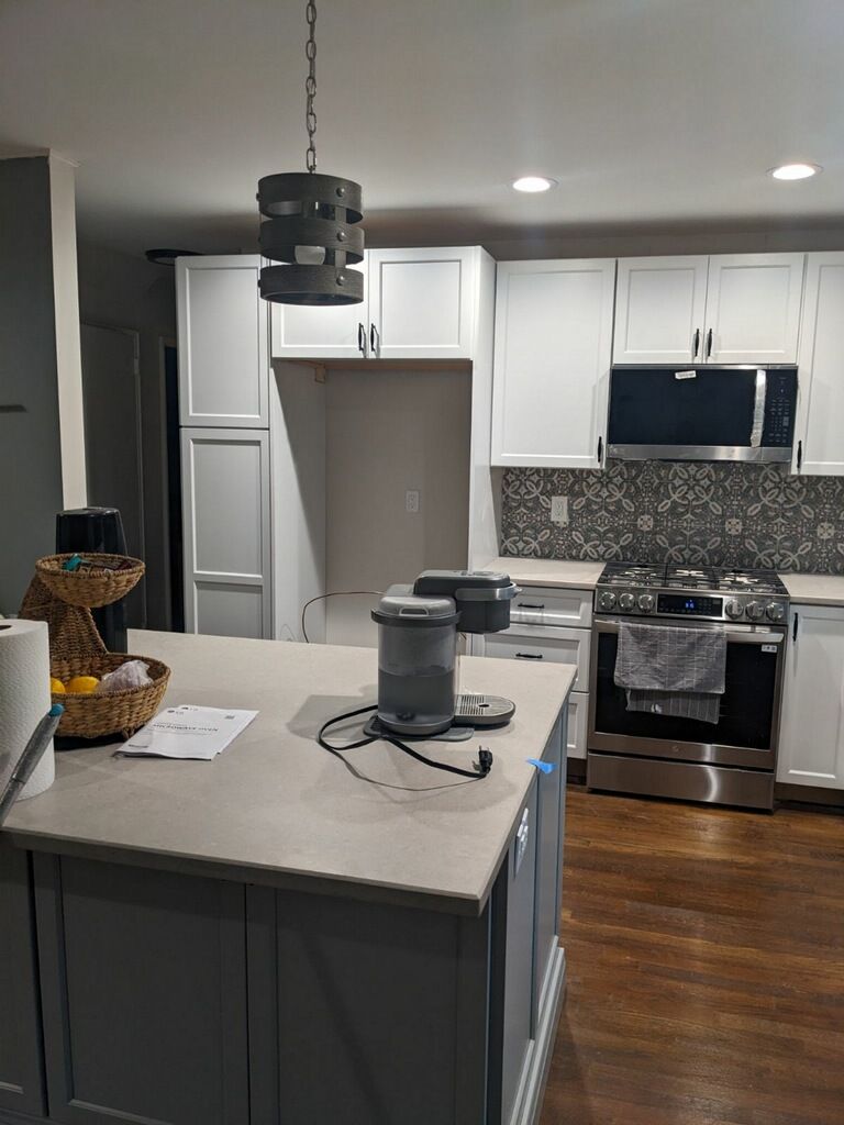 Kitchen with white cabinets, gray island, stainless steel appliances, and a hanging light fixture.