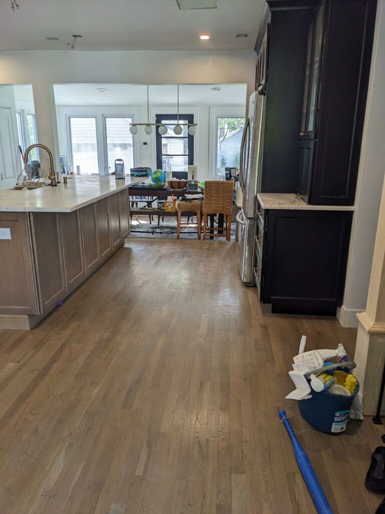 Kitchen with hardwood floors, island, black cabinets, and a view into a dining area.