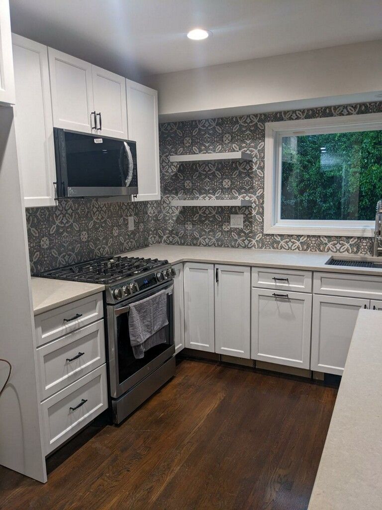White kitchen with dark wood floors, stainless steel appliances, and a mosaic backsplash.