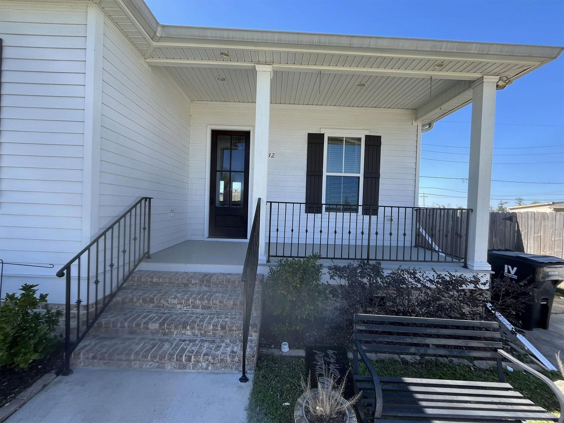 White house with porch, steps, black door, and shutters, railing. Sunny day.