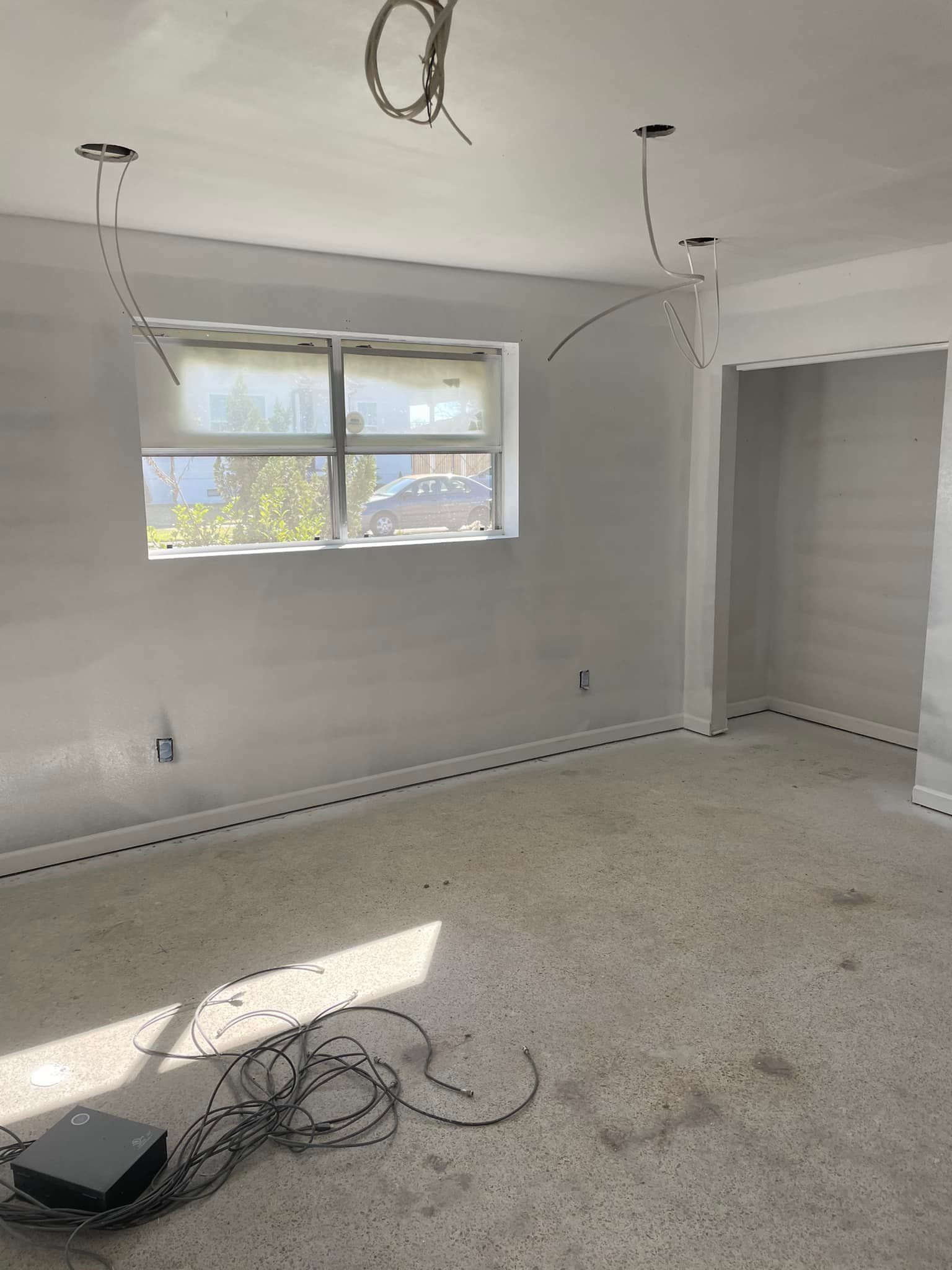 Room with exposed electrical wiring, unfinished walls, window, and exposed aggregate flooring.