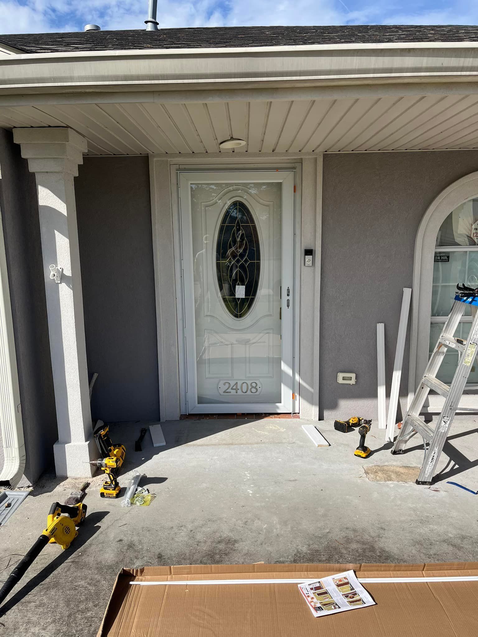 White entry door with oval window, on a porch. Tools and materials nearby.