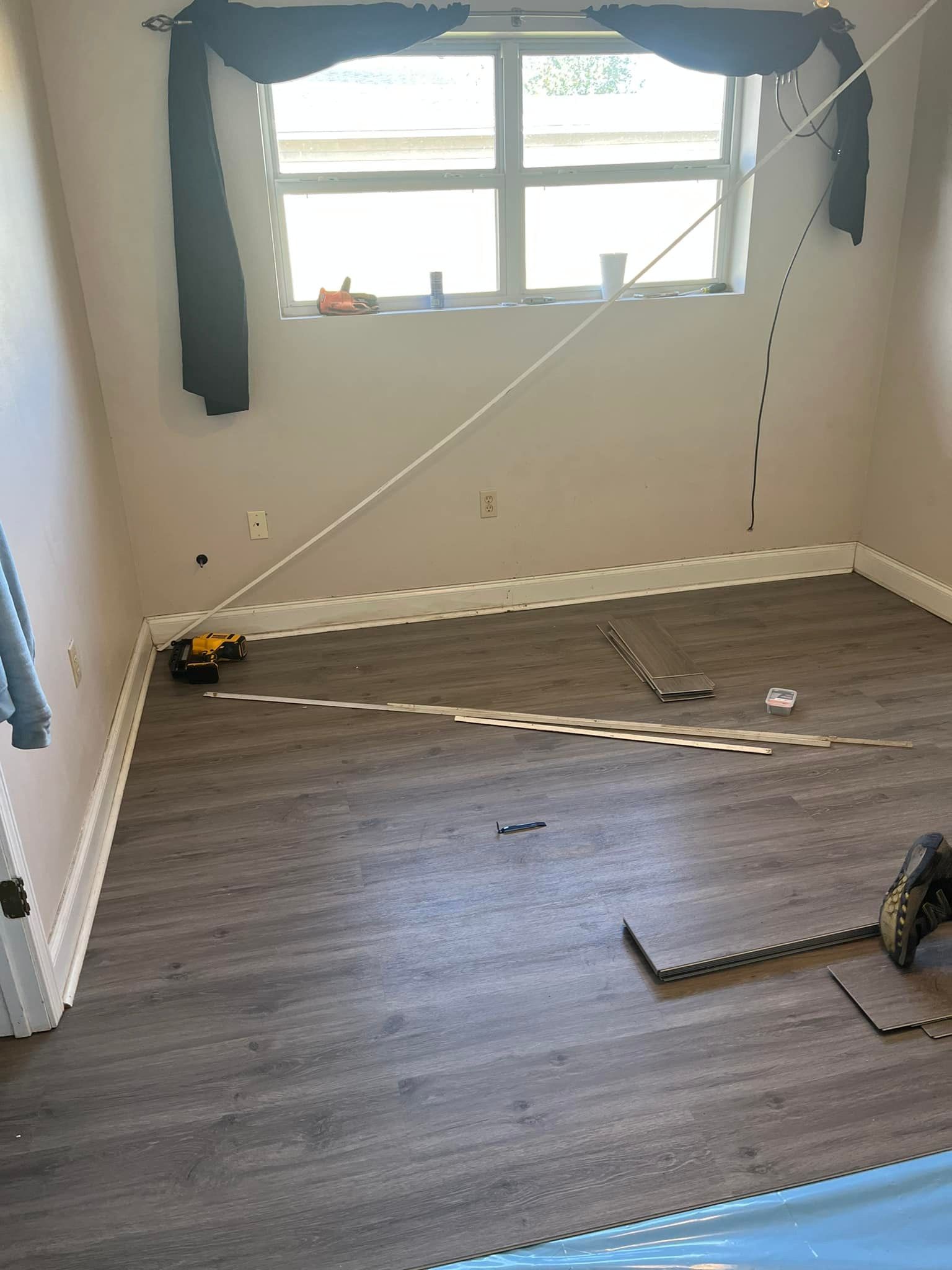 Room with grey laminate flooring being installed, with tools and a window.