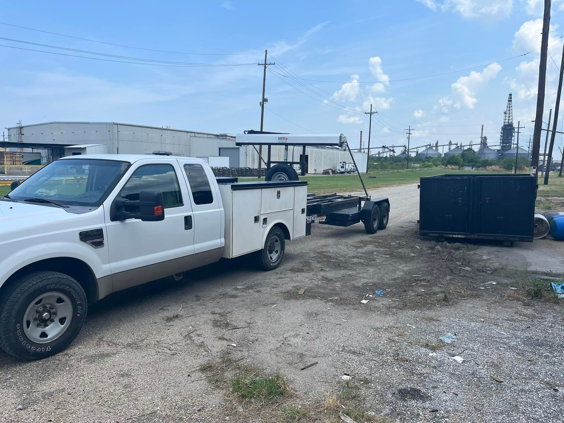 White work truck towing a trailer with a black generator on gravel under a cloudy sky.
