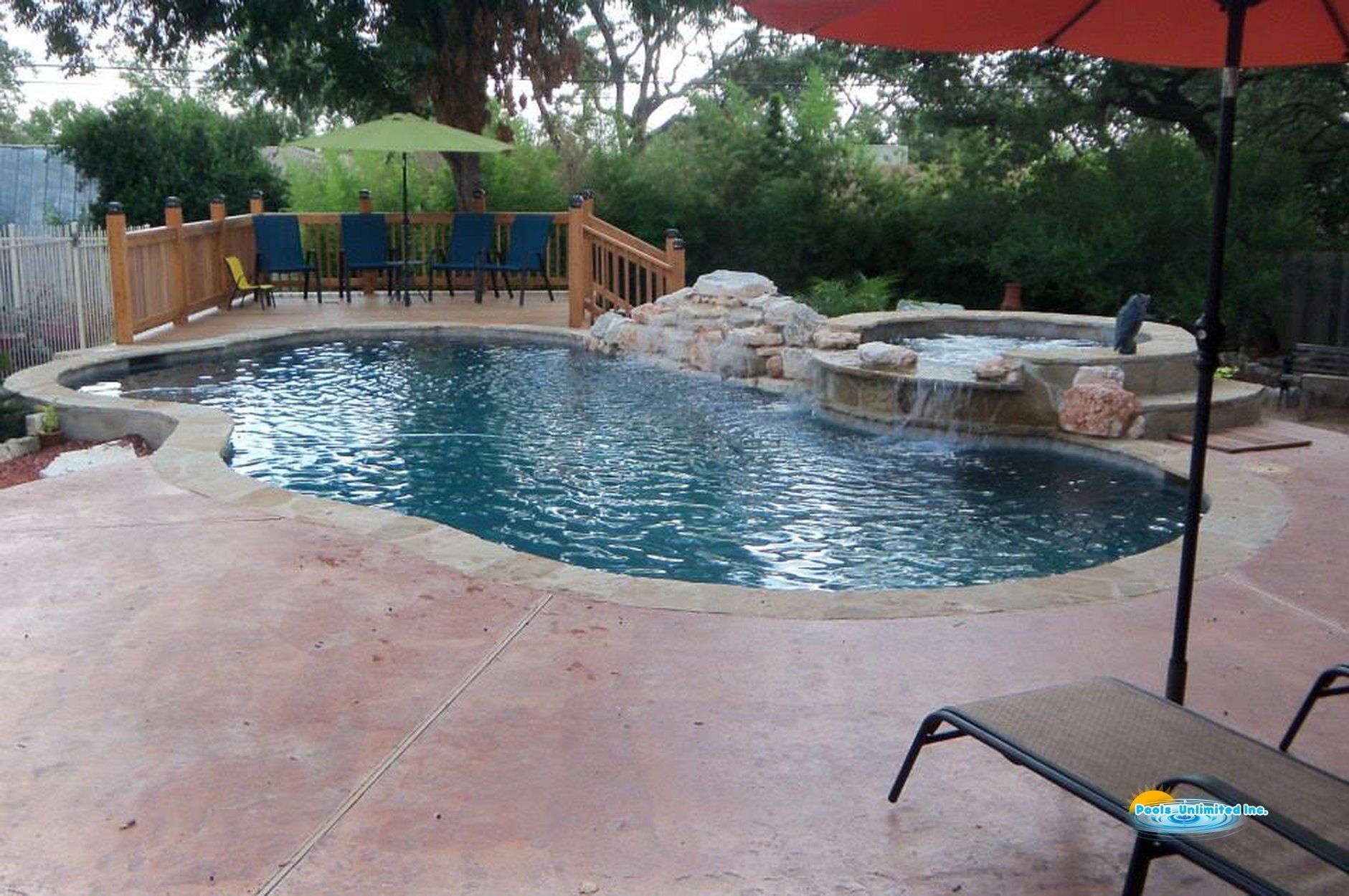 A large swimming pool with a hot tub in the middle of it surrounded by trees.