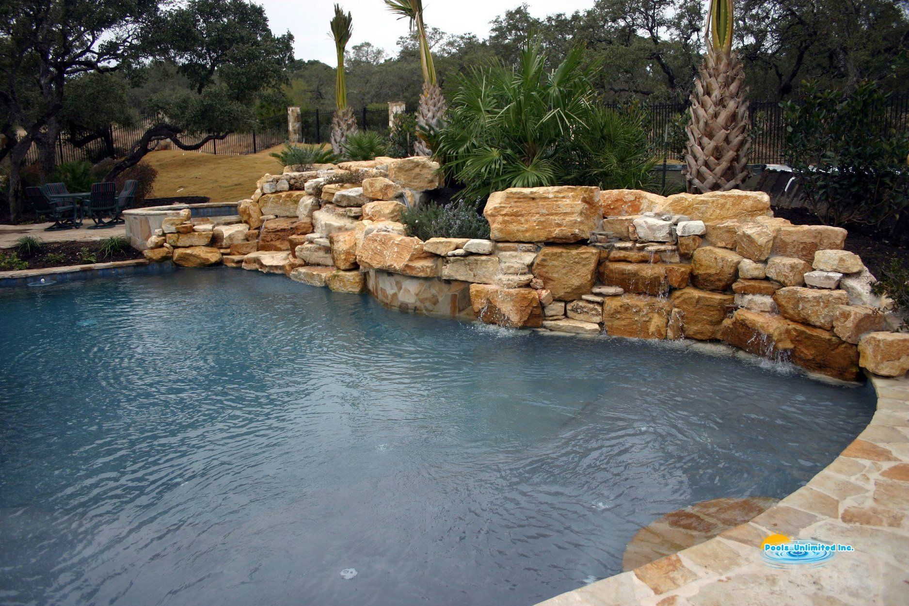 A large swimming pool with a waterfall in the backyard of a house.