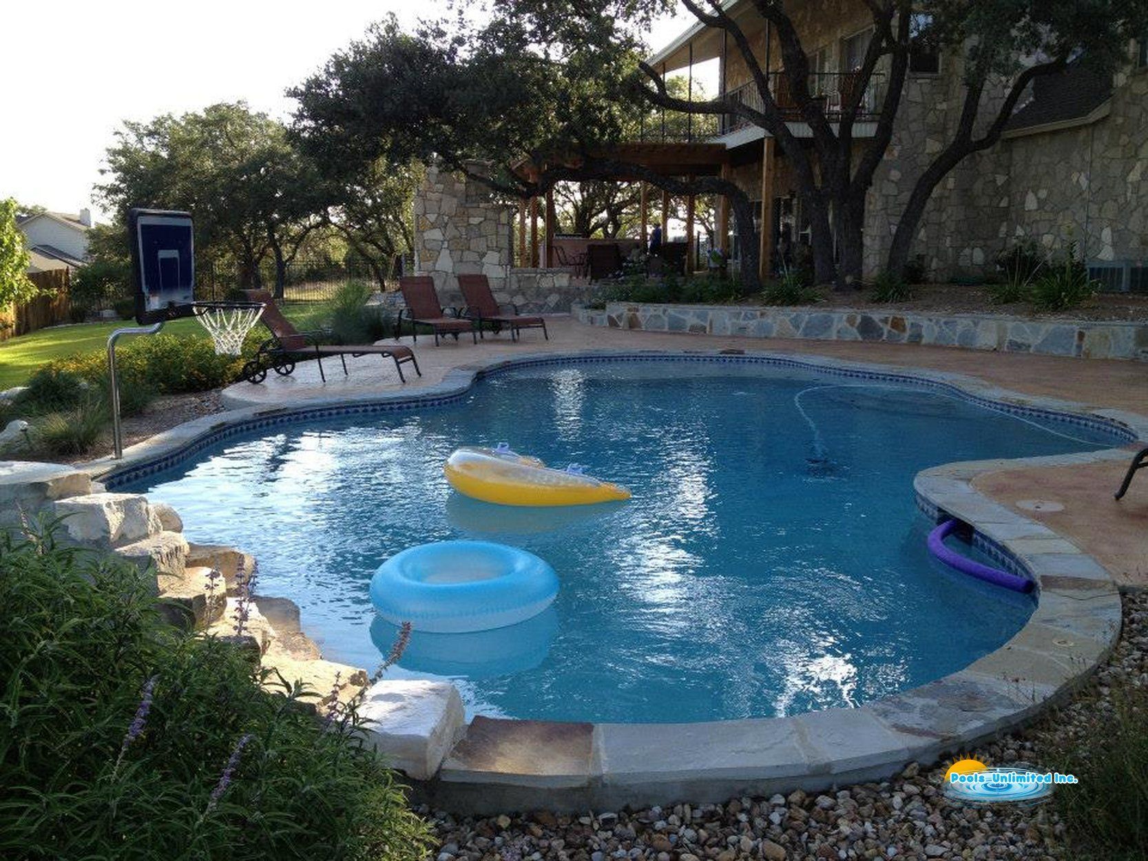 A large swimming pool is surrounded by trees and a table and chairs.