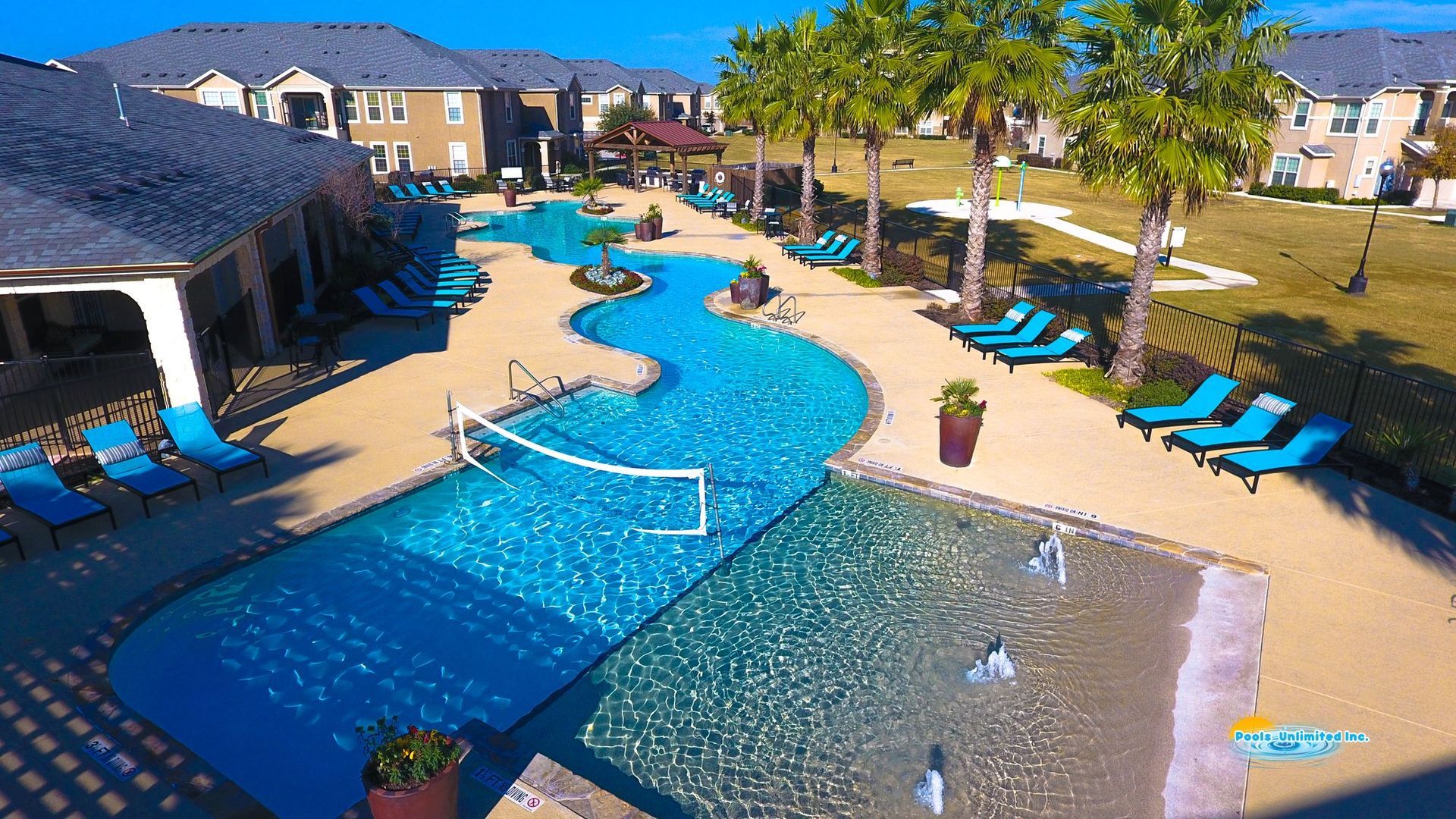 An aerial view of a large swimming pool surrounded by chairs and palm trees.