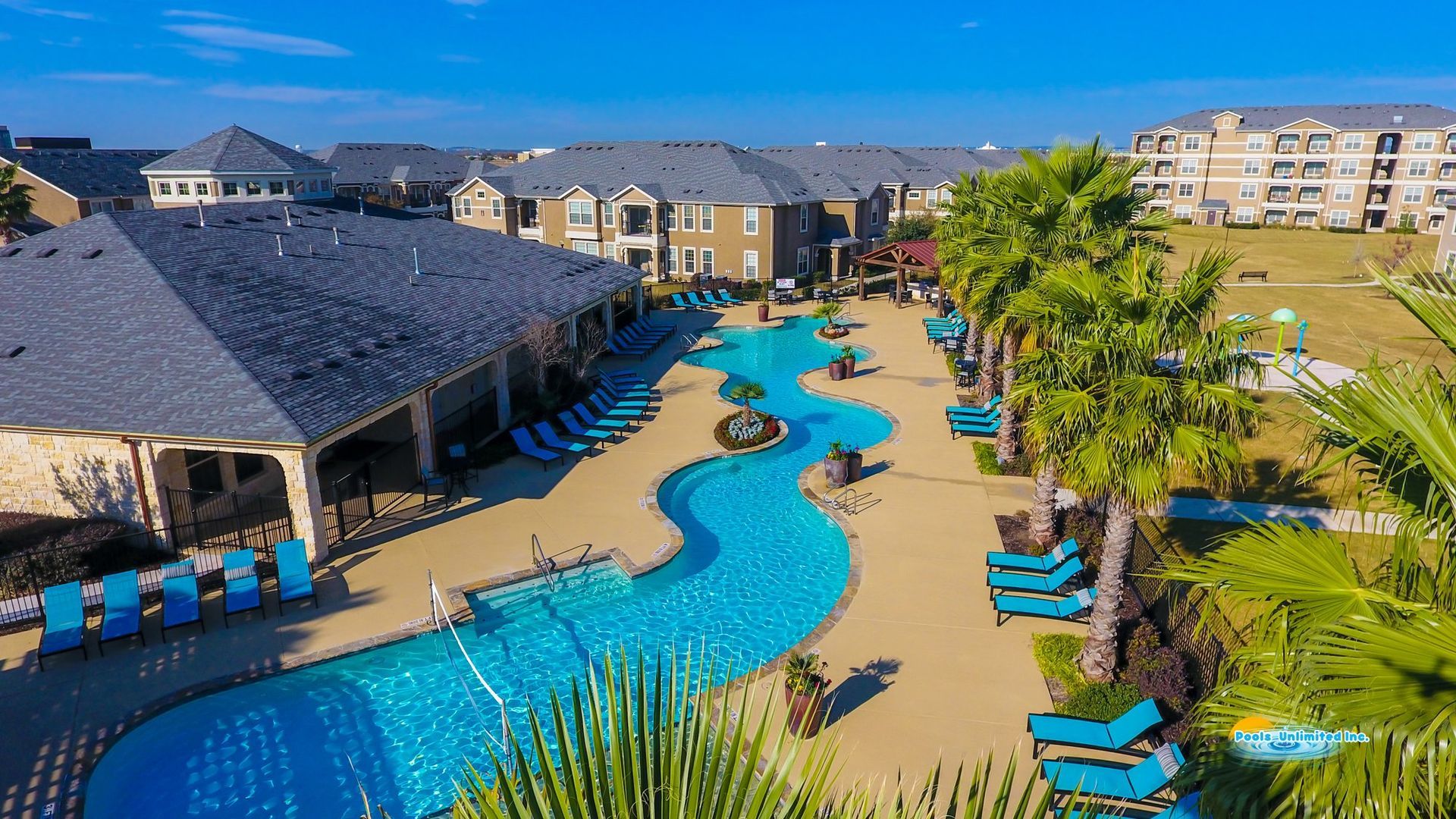 An aerial view of a large swimming pool surrounded by palm trees and chairs.