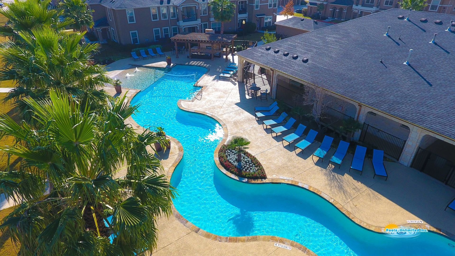 An aerial view of a large swimming pool surrounded by chairs and palm trees.