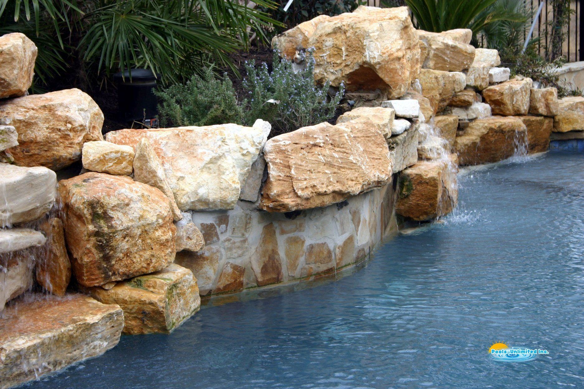 A large rock wall surrounds a swimming pool with a waterfall.