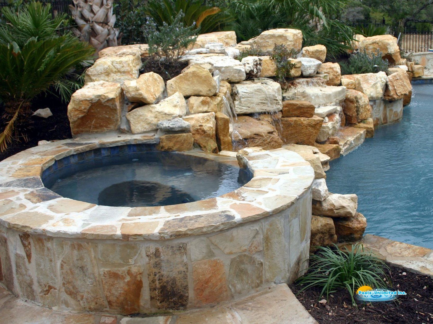 A hot tub surrounded by rocks next to a swimming pool.