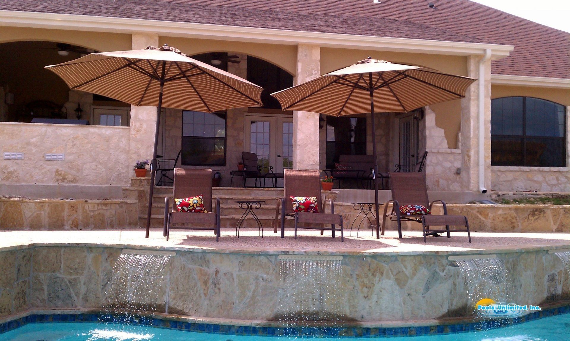 A swimming pool with chairs and umbrellas in front of a house