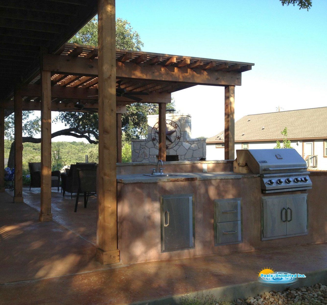 An outdoor kitchen with a grill under a pergola