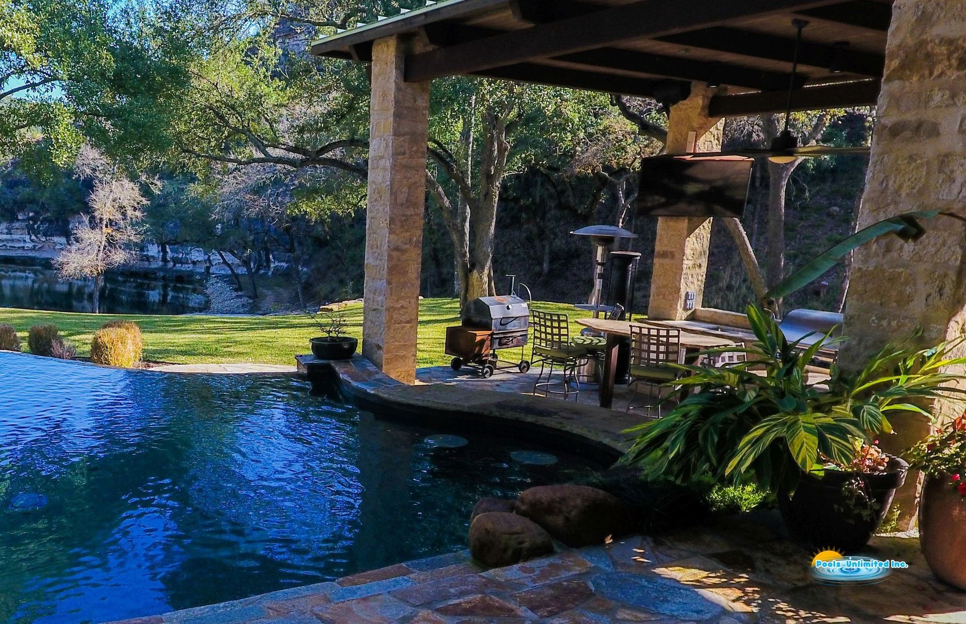A large swimming pool is surrounded by a stone patio and covered patio area.