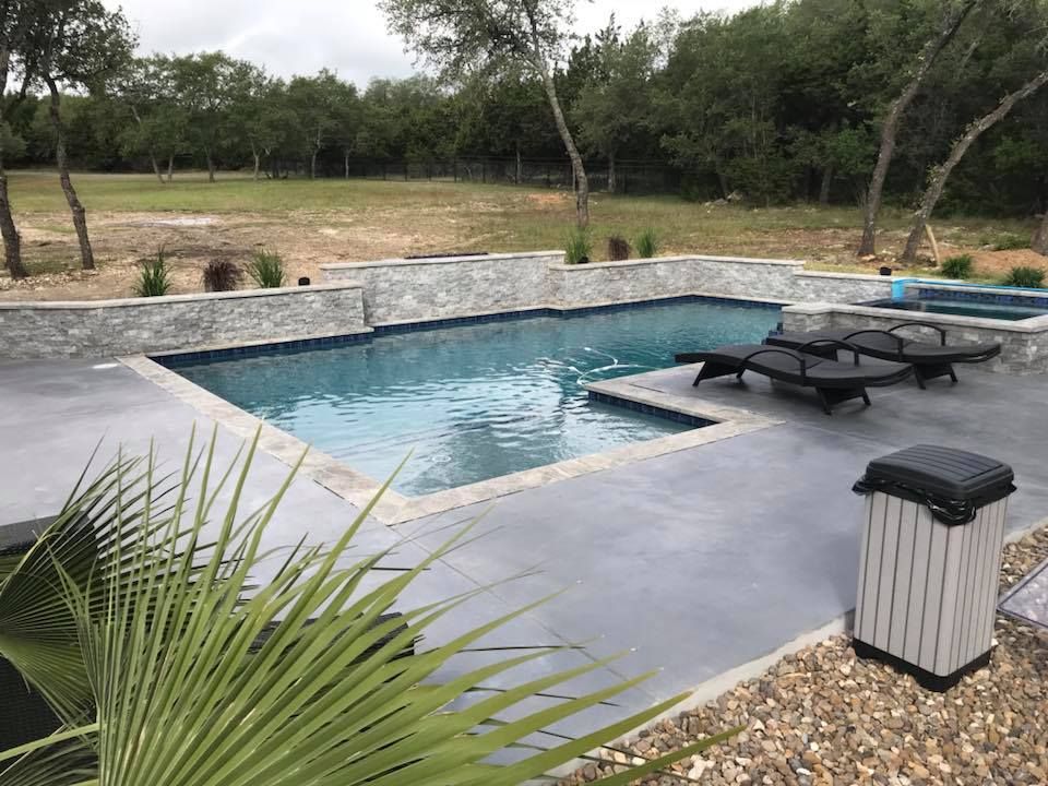 A large swimming pool surrounded by lawn chairs and a trash can.