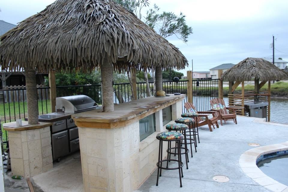 A patio with a thatched roof and a grill