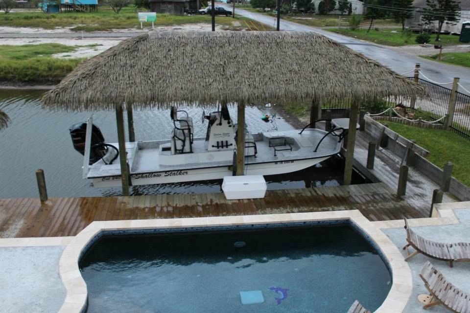 A boat is docked under a thatched roof next to a pool