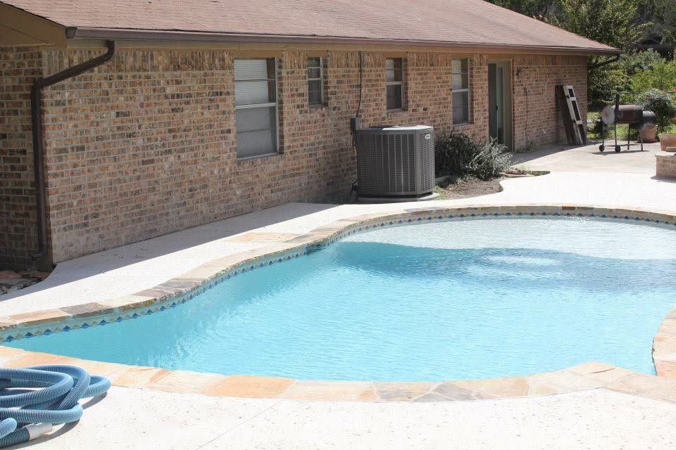 A large swimming pool in front of a brick house