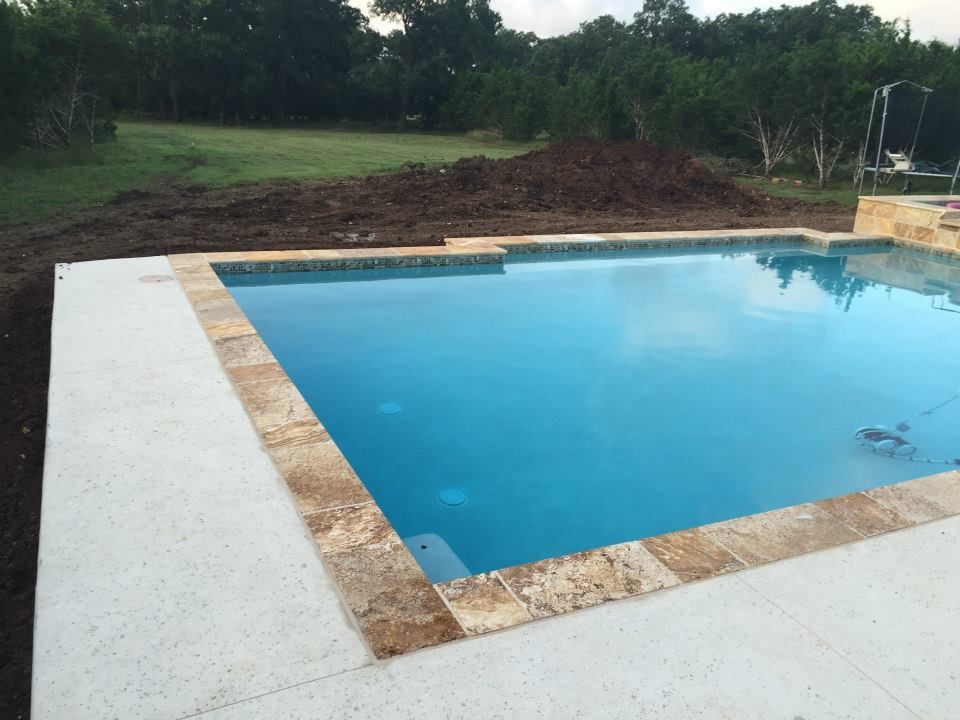 A large swimming pool is surrounded by dirt and trees.