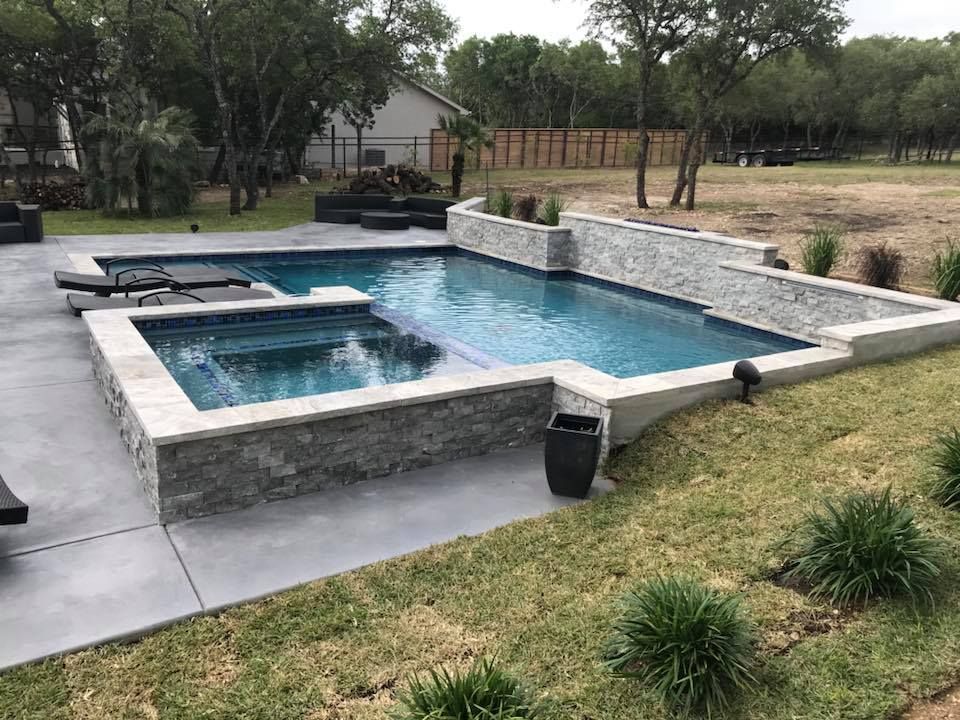A large swimming pool is surrounded by a stone wall in a backyard.