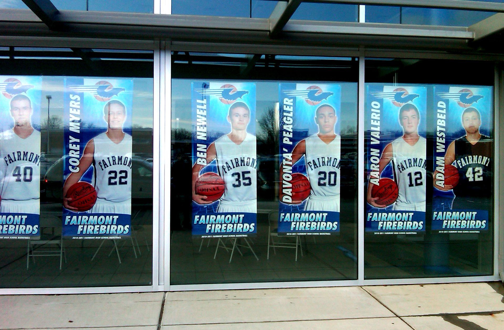 Posters of Fairmont Firebirds basketball players in a window. Names include: Corey Myers, Ben Newell, Davonta Peagler, and more.