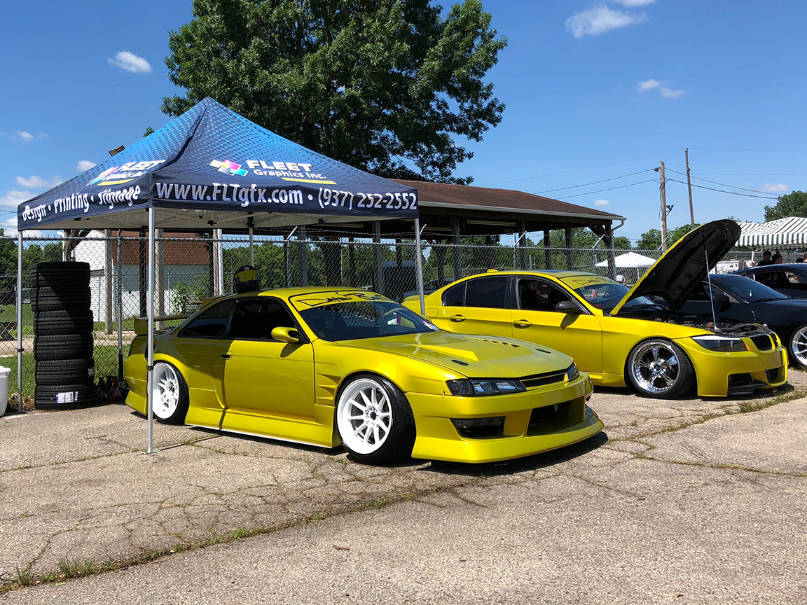 Yellow drift cars parked under a tent on a sunny day.